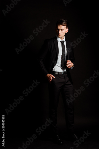 handsome businessman in suit standing with hand in pocket on black