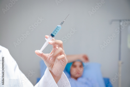 The female doctor prepared a syringe to treat the patient lying on the bed.