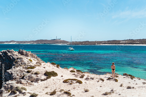 Woman in bikini  on a bright summers day at the beach looking out admiring the view of the stunning ocean and a white boat  at a bay on Rottnest Island  Western Australia.