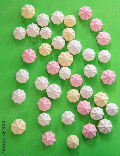 Flat lay of pastel colered meringue desserts in a random pattern on a vibrant green background