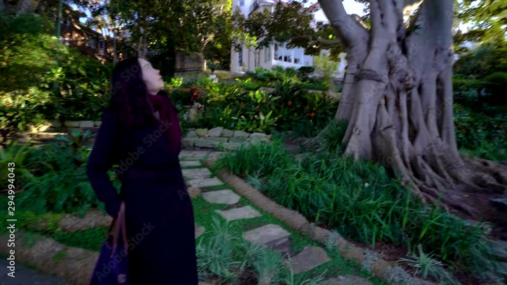 Beautiful girl walking down a path through a garden, she stops and turns her head to notice the blossoms Beautiful girl walking down a path through a garden, she stops and turns her head to notice the blossoms