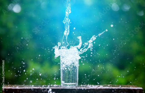 Drink water pouring in to glass over sunlight and natural green background.Select focus blurred background.