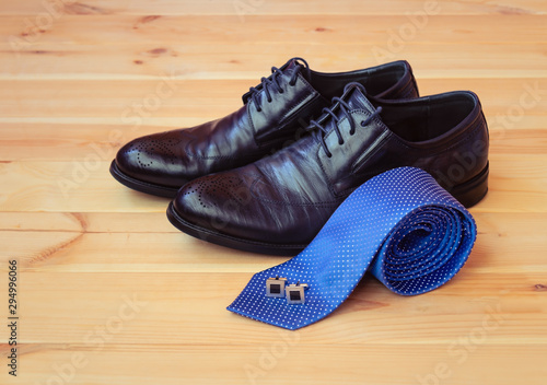 Blue rolled necktie, cufflinks and fashionable black men's shoes on wooden background. Selective focus.
