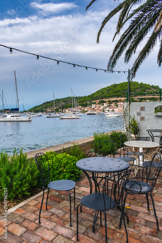 A beautiful Mediterranean beach bar terrace empty after rain decorated with flowers  palm trees and lights with a view of sailing boats in the port of Vis   Vis island  Croatia  Europe. Summer travel