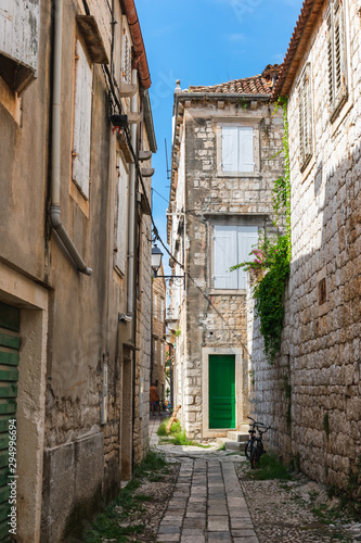 Beautiful view of a narrow Mediterranean street with stone houses with green doors and wooden shutters and mediterranean plants. Vis island, Croatia, Europe. Summer and travel concept.