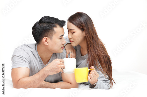 Lovers lying on the bed holding a cup of coffee Talk happily in the bedroom. White background. The concept of a newly married couple