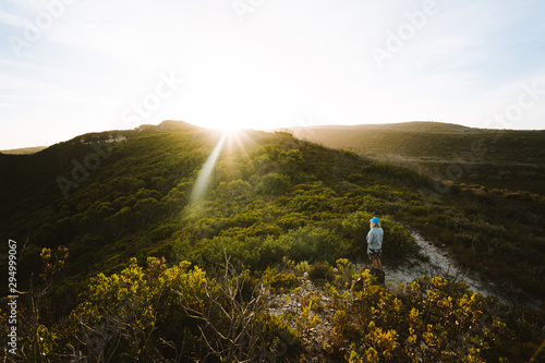 Lone woman admiring the sun rays at sunset over the mountains and trees on an evening hike near Shelley Beach in Albany, Western Australia.