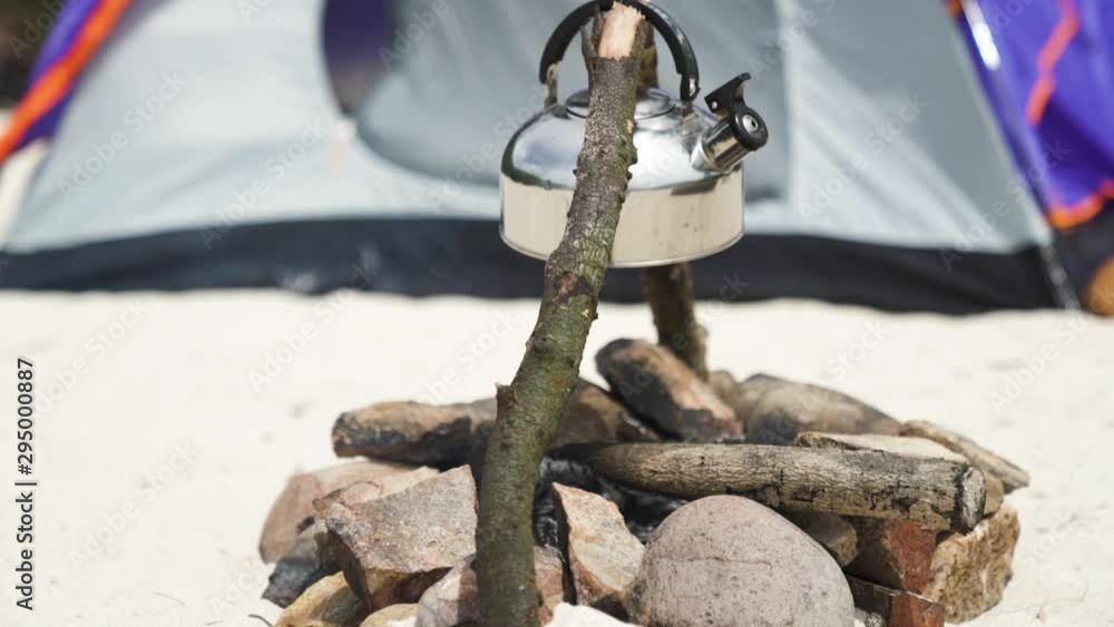 An aluminium kettle hanging over a pile of wood, campfire on the beach. An aluminium kettle hanging over a pile of wood, campfire on the beach.