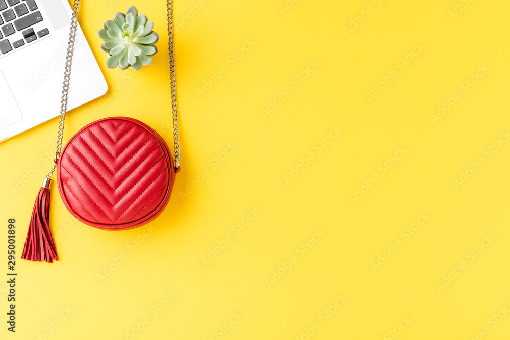 Fashion background with red woman’s purse with laptop and small green succulent on yellow desktop Fashion background with red woman’s purse with laptop and small green succulent on yellow desktop