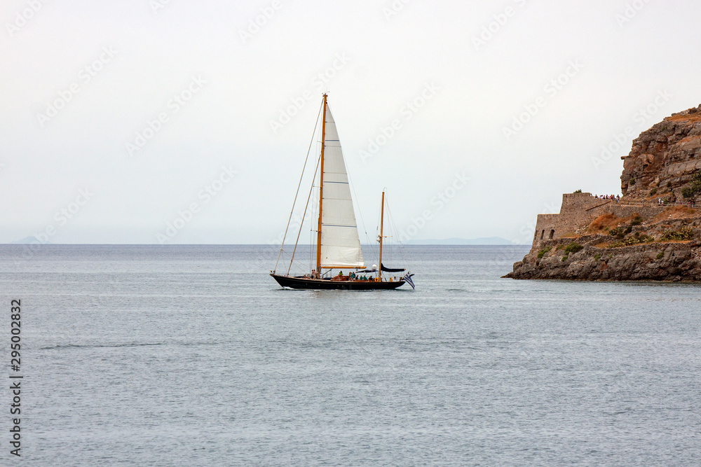 sailboat passes in front of the island of Spinalonga; Crete, Greece sailboat passes in front of the island of Spinalonga; Crete, Greece