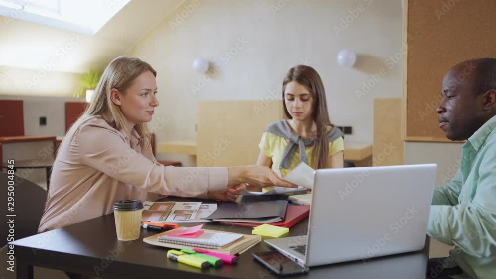 Lady in casual outfit sharing documents with colleagues then sipping hot beverage and starting discussion of software UI design in office Lady in casual outfit sharing documents with colleagues then sipping hot beverage and starting discussion of software UI design in office