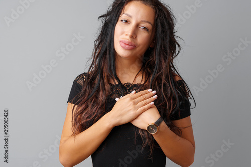 Young brunette woman touching her heart with her hands over gray background.