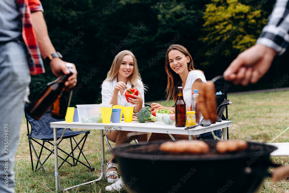 Smiling women sitting at the table with fresh food and looking on the barbecue