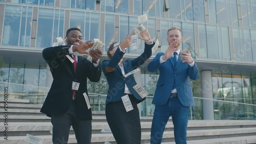 Diverse group of rich businessmen throw handful of banknotes in the air. Multiracial businessmen fooling around, throw cash in front of office building photo