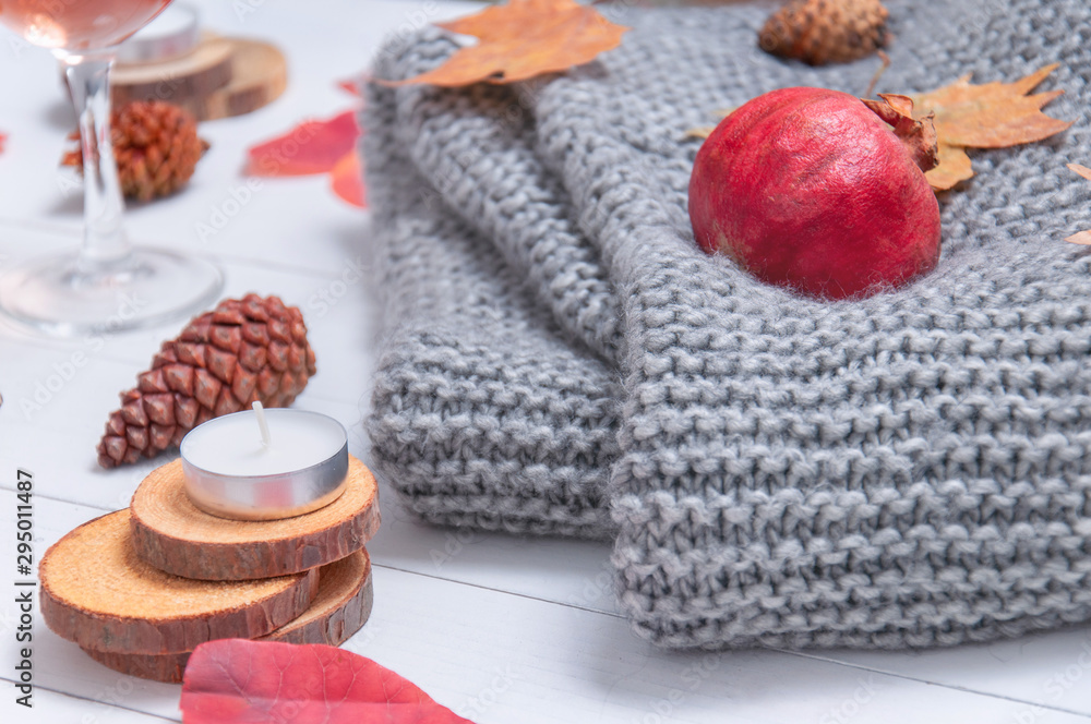 Small candles, two glasses with rose wine, cones, dry red leaves, a gray scarf knitted on a white wooden table. Hello, Autumn. Cozy autumn background. Small candles, two glasses with rose wine, cones, dry red leaves, a gray scarf knitted on a white wooden table. Hello, Autumn. Cozy autumn background.