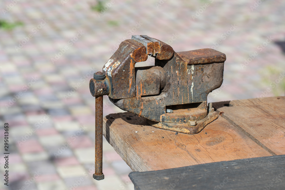 Old rusty vise for metal products on wooden table, outdoors, close up Old rusty vise for metal products on wooden table, outdoors, close up