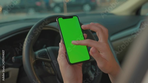 Female driver sitting in the car browsing online map on vertical mock-up smartphone greenscreen searching route planning a roadtrip. Lifestyle and technology.