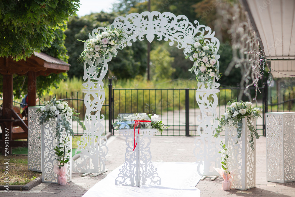 Wedding white wooden arch decorated with flowers outdoors. Beautiful wedding set up. Wedding ceremony on green lawn in the garden. Part of the festive decor, floral arrangement. Horizontal photo.