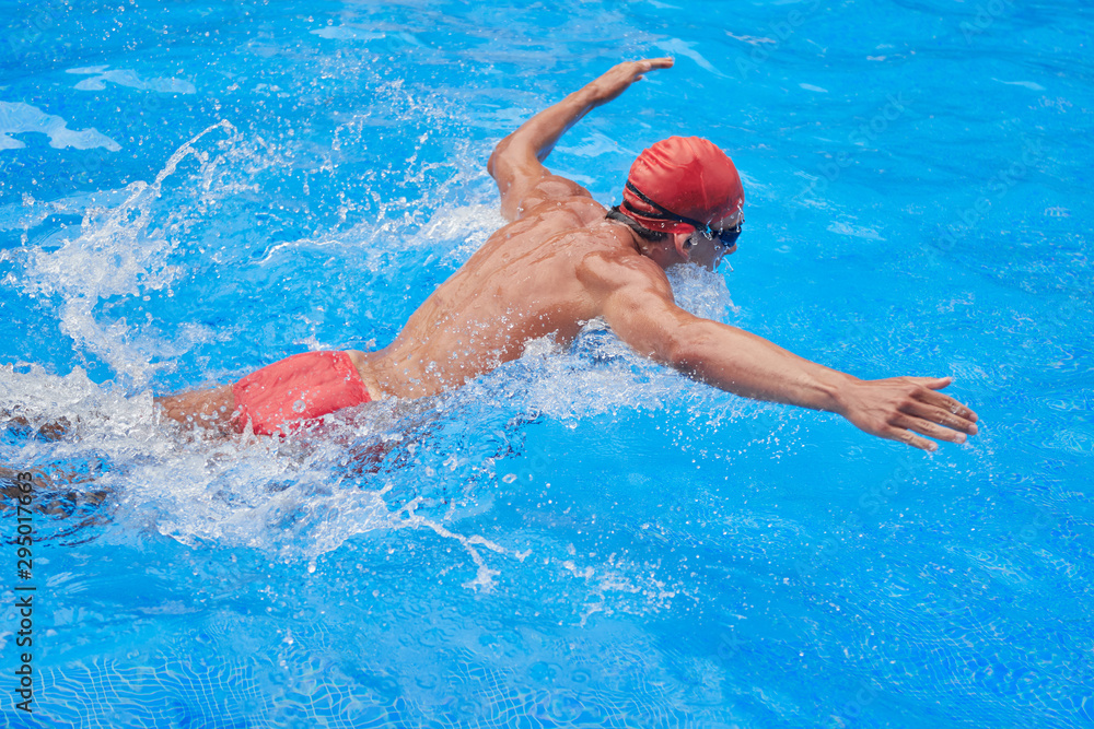 Swimmer in an outdoor pool, swimming butterfly-style, with open arms, seen from the side