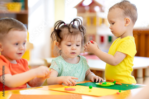 Three children toddlers playing with plasticine in nursery or creche