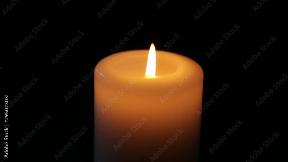 a large candle burns in the dark. White candle. Black background. close up a large candle burns in the dark. White candle. Black background. close up