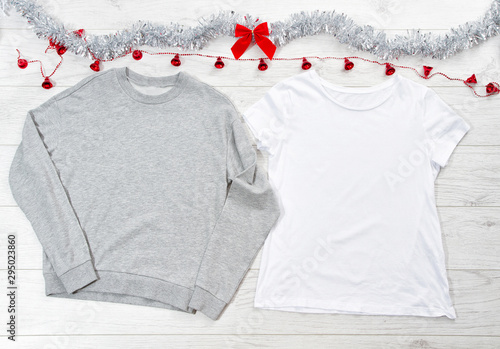 Close up white blank template t shirt, gray sweatshirt hoodie with copy space and Christmas Holiday concept. Top view mockup t-shirt, red bow on white wooden background. Happy New Year decorations © ladyalex
