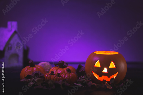 Halloween pumpkin head Jack lantern next to several pumpkins and a house on purple background
