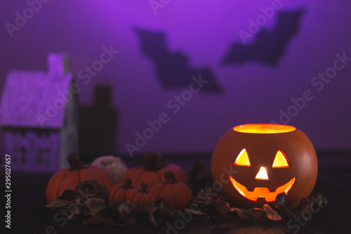 Halloween pumpkin Jack lantern next to several pumpkins and a house on purple background with bats