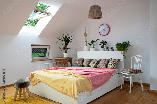 Modern and cozy interior of bedroom with white furniture and wooden floor. Pattern pillows and colorful bedspread on the double bed. Eco style. photo