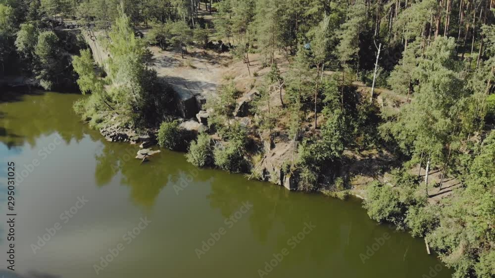 Aerial view of a rocky cliff on the edge of a high mountain lake with coniferous forest and a tourist tent on the shore Aerial view of a rocky cliff on the edge of a high mountain lake with coniferous forest and a tourist tent on the shore