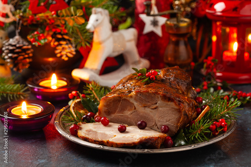 Roast pork neck in Christmas style. Dark navy blue background. Christmas accessories. Candles and lanterns in the background. photo