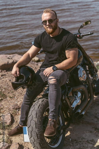 Sexy bearded biker lying on his motorcycle holding helmet