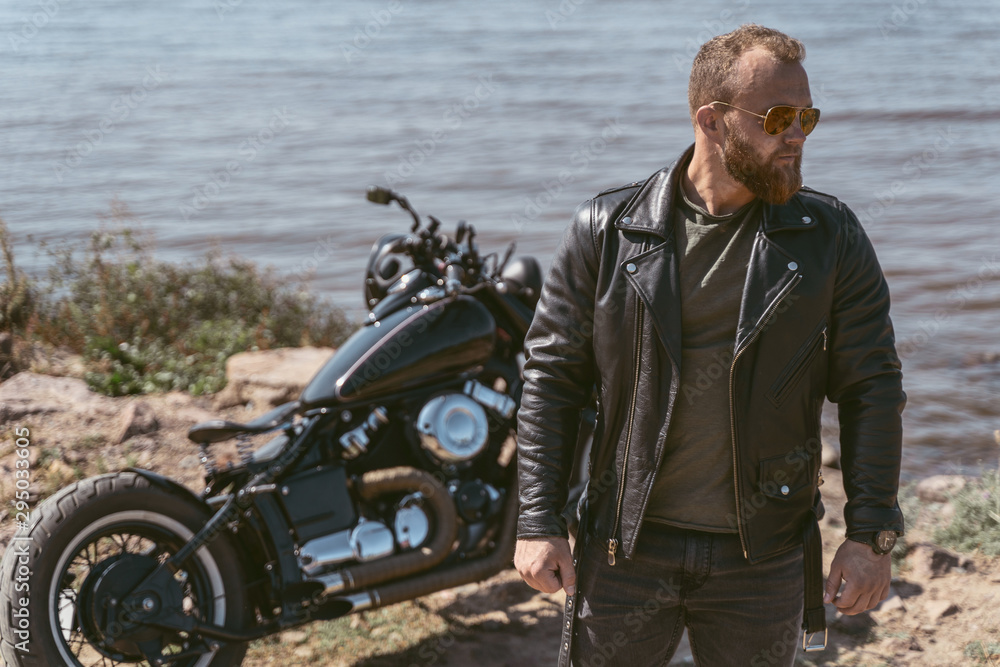 Handsome bearded biker posing near his motorcycle