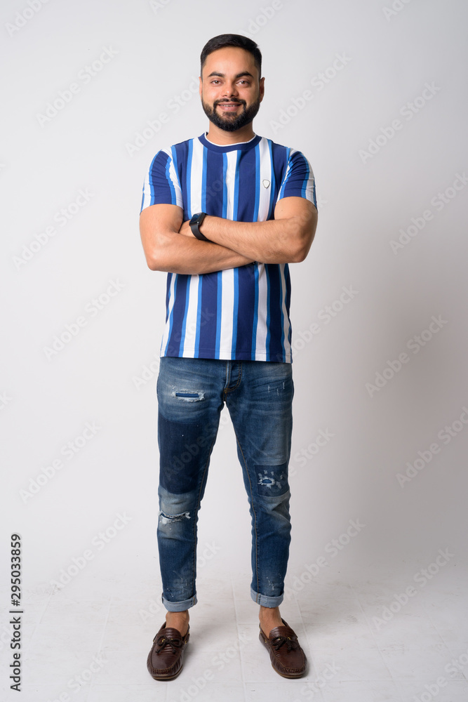 Full body shot of happy young bearded Indian man smiling with arms crossed Full body shot of happy young bearded Indian man smiling with arms crossed