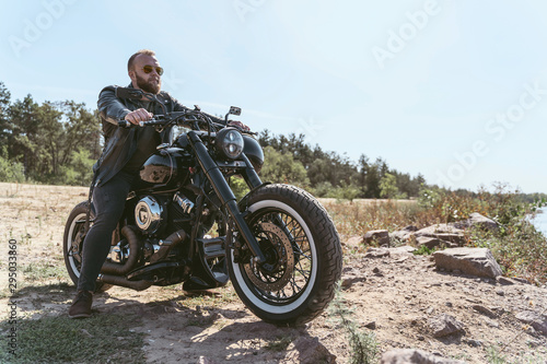 Handsome bearded biker in leather jacket sitting on his bike
