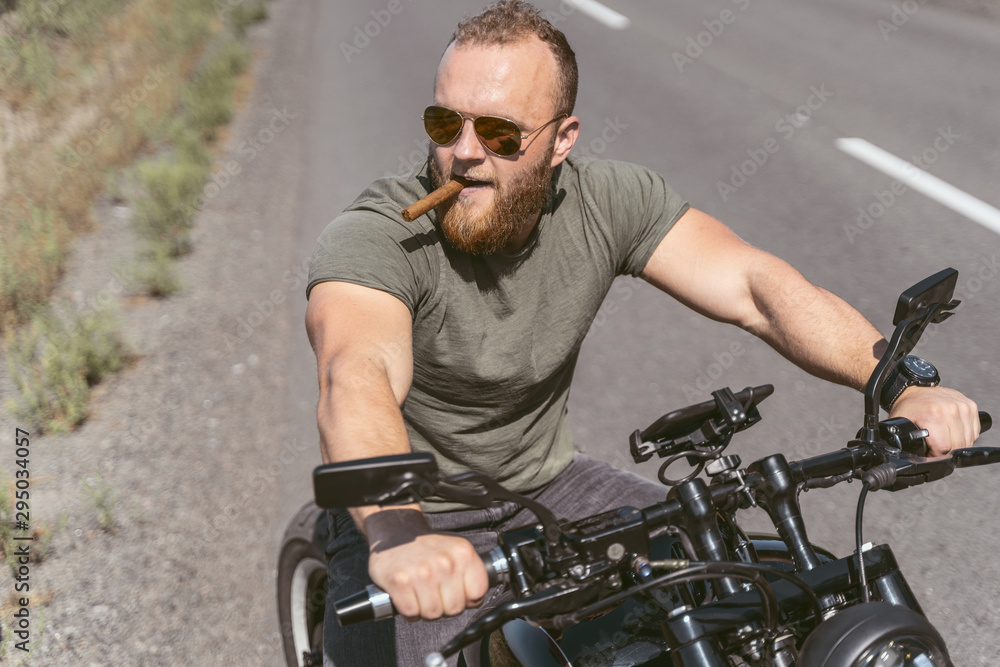 Handsome bearded biker sitting on bike smoking sigar on the road