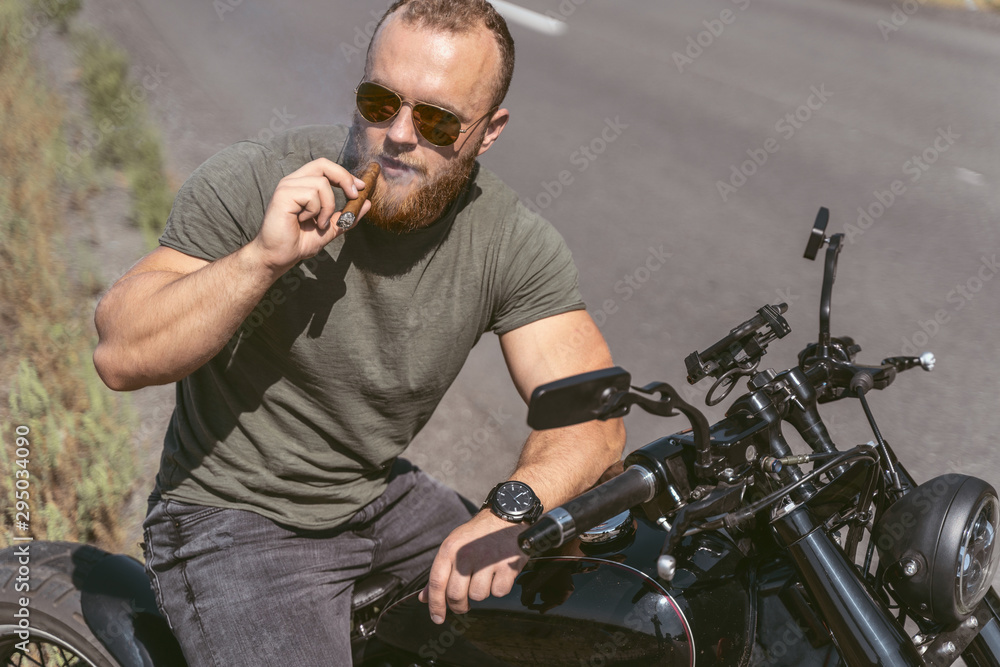 Confident bearded biker with sigar posing on bike Confident bearded biker with sigar posing on bike