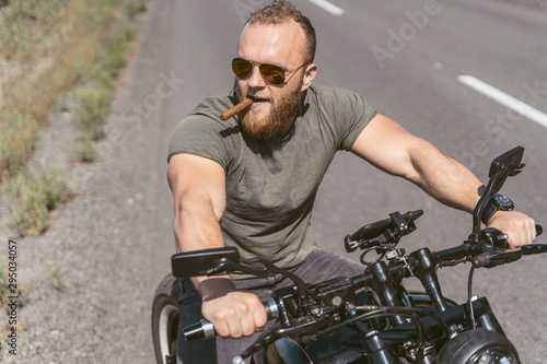 Handsome bearded biker sitting on bike smoking sigar on the road