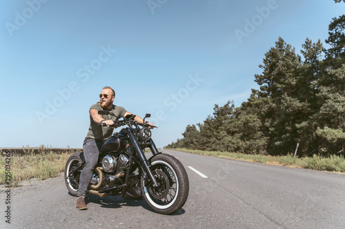 Fototapeta Naklejka Na Ścianę i Meble -  Handsome bearded biker posing on his bike wearing sunglasses