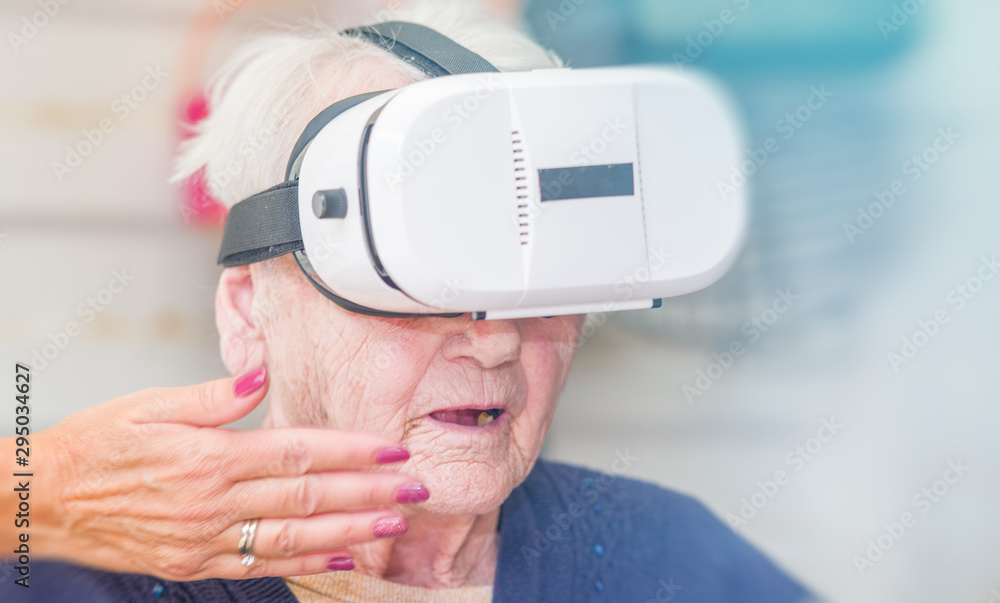 Amazed face of a elderly retired woman on the wheelchair using VR glasses. Virtual reality experience