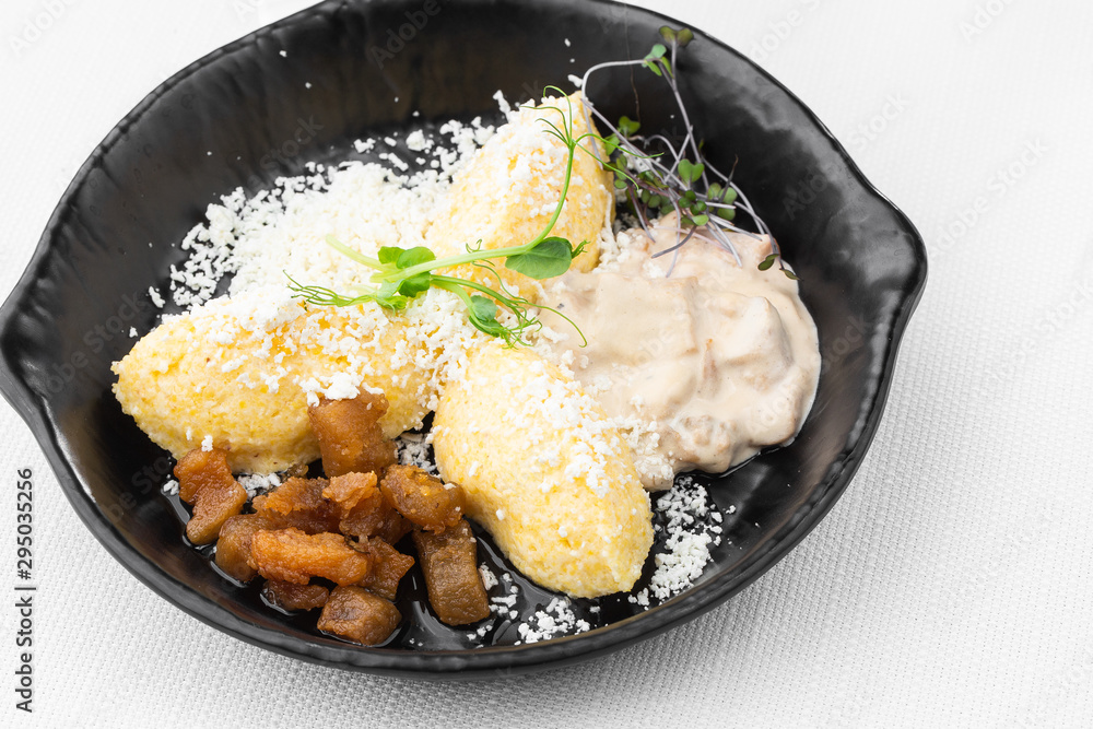 Typical Ukrainian dish polenta - Banosh with cheese, lard and white mushrooms. Maize porridge with bacon, cracklings and cheese. Corn porridge in black pan on white background. Horizontal photo.