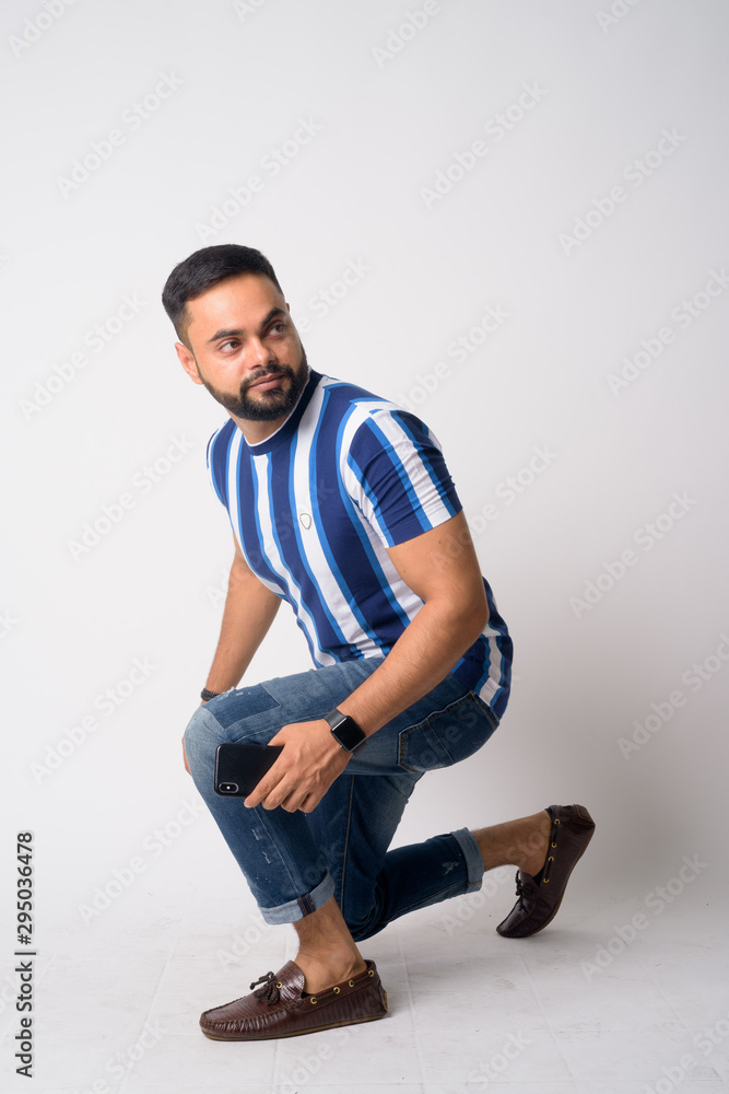 Full body shot of young bearded Indian man crouching Full body shot of young bearded Indian man crouching
