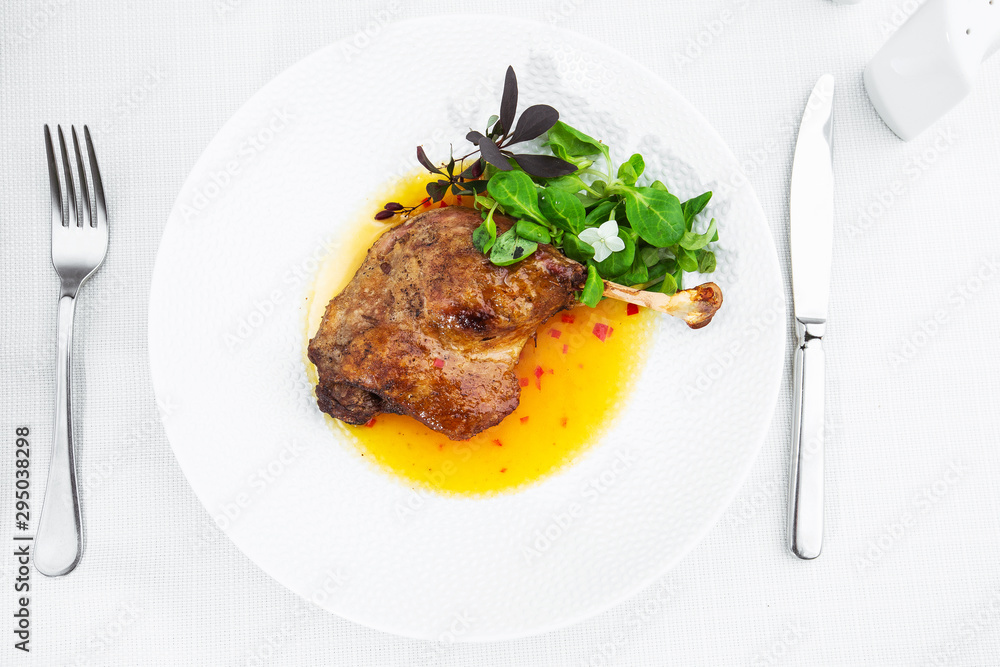 Roast duck leg with mango sauce, salade and chilli pepper on white plate, closeup. Horizontal view from above, top shot. White background.