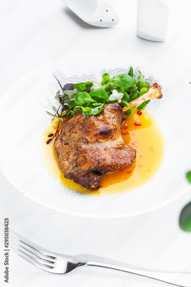 Roast duck leg with mango sauce, salade and chilli pepper on white plate, closeup. Vertical view from above, top shot. White background.