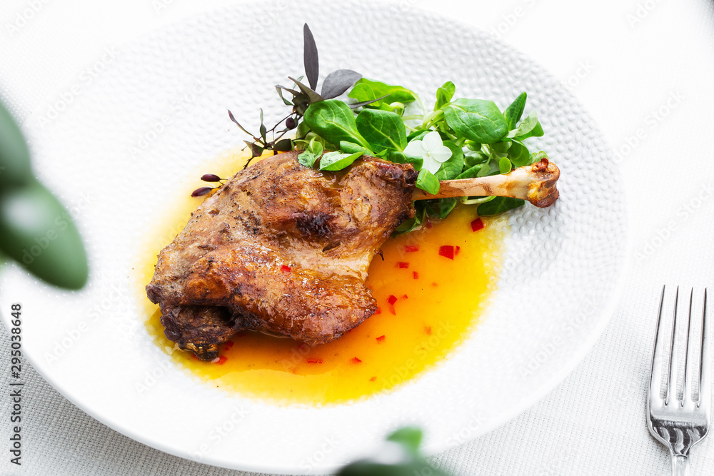 Roast duck leg with mango sauce, salade and chilli pepper on white plate, closeup. Horizontal view from above, top shot. White background.