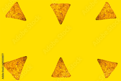 Abstract bright background of whole triangular nachos slices on yellow color with an empty space in the center