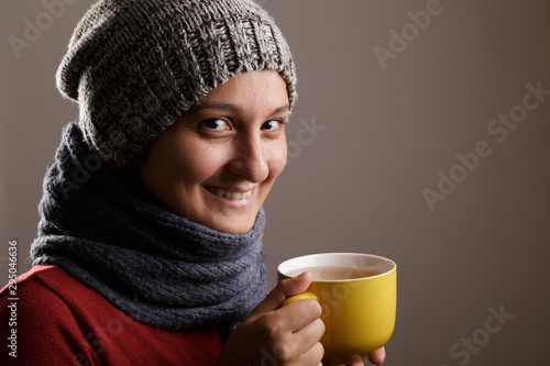 Young woman wearing a woolen scarf and a cap drinking hot tea. Autumn and winter season and illness concept.