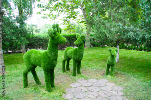 Sculptures of three deer in full face in the Park green on the background of trees.