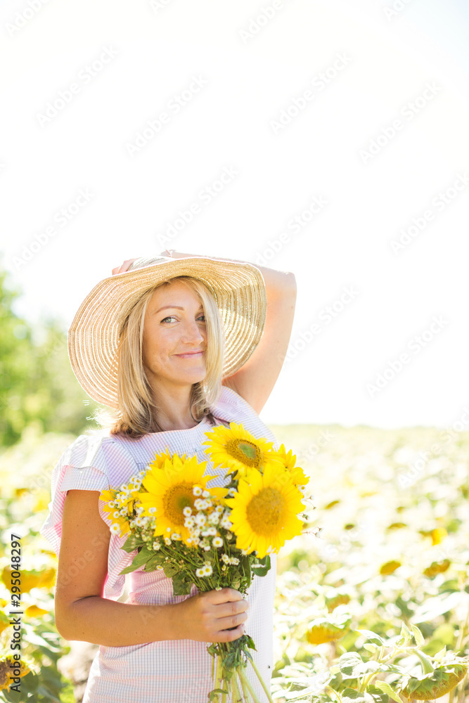 A blonde woman in a pink dress in a field with sunflowers. A woman holds a bouquet of sunflowers in her hand