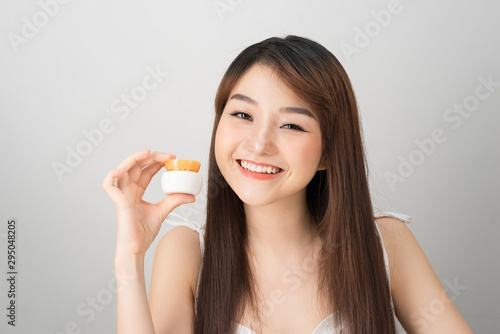 Smiling young asian woman showing skincare product. Beauty concept.